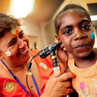 A health practitioner checks the ear of a young Indigenous girl.